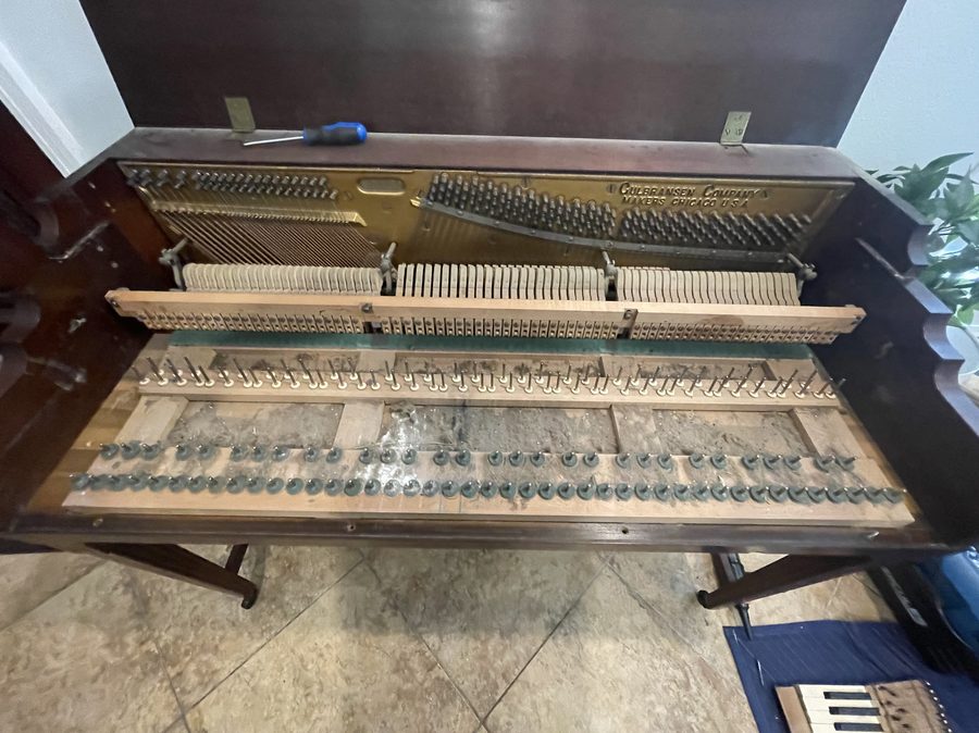 Inside of an upright piano before cleaning — dusty wooden surfaces and aged action parts